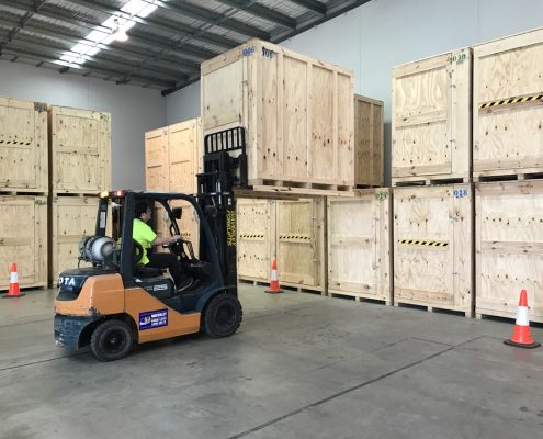 Office movers Melbourne — forklift operator moving large timber crates inside a commercial warehouse facility.