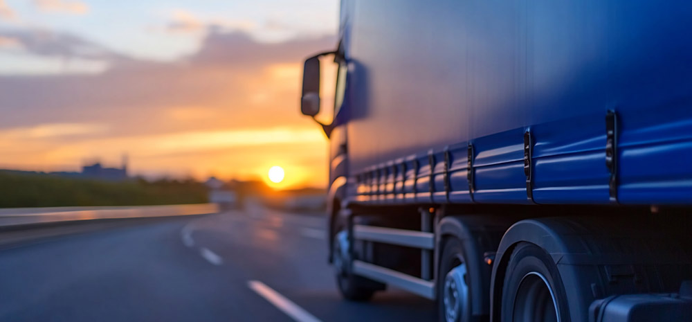 A blue moving truck driving on a highway at dusk, symbolizing the frequent transit handled by a Melbourne to Sydney removalist.